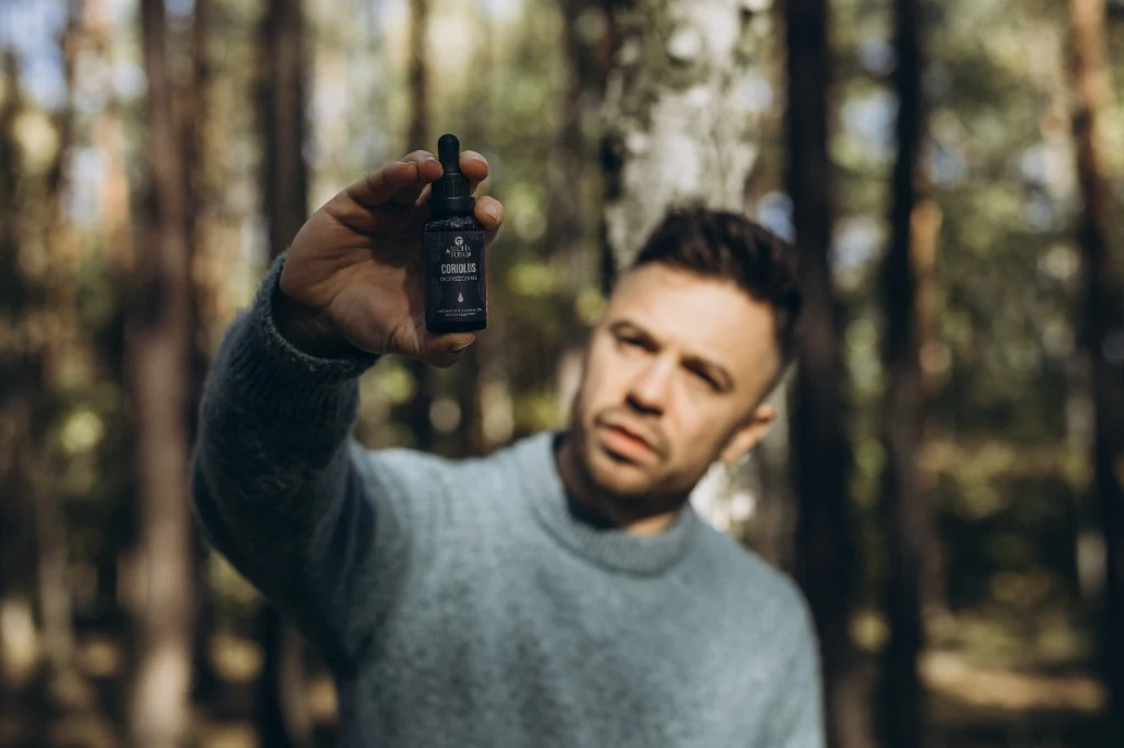 Mateusz Rosa trzyma butelkę Coriolus w lesie · produkt zgodny z rytmami natury